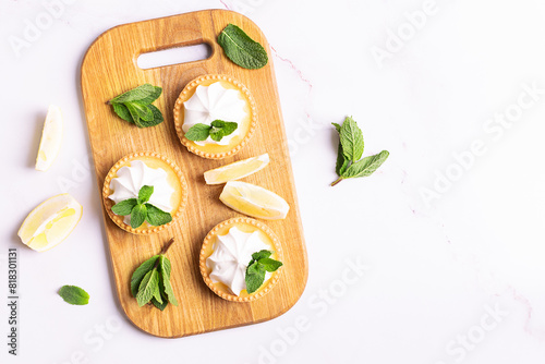 Aromatic homemade lemon tartlets with cream and mint leaves on white marble table top view.