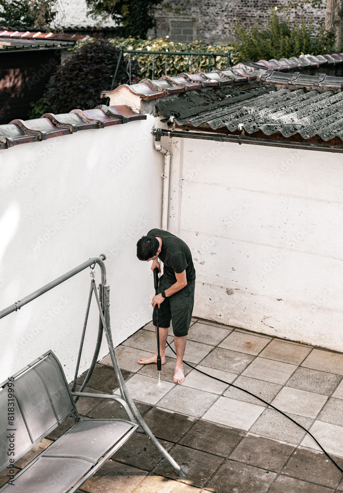 A young guy washes his backyard with a kercher. A young guy washes his backyard with a kercher.