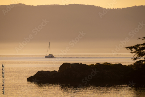 Sailboat in Hale Passage passing by Abner Point during a beautiful sunrise. Seen from the Aiston Preserve on Lummi Island with Bellingham Bay in the background. 