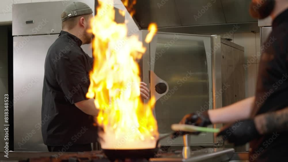 Active work in the kitchen in a restaurant a chef uses alcohol to light a fire in a frying pan while his colleague takes out the finished baked goods from the oven in the kitchen in a restaurant Active work in the kitchen in a restaurant a chef uses alcohol to light a fire in a frying pan while his colleague takes out the finished baked goods from the oven in the kitchen in a restaurant