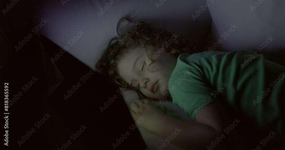 A young boy peacefully sleeps on a couch with a digital tablet by his side, illuminated by soft lighting. A young boy peacefully sleeps on a couch with a digital tablet by his side, illuminated by soft lighting.