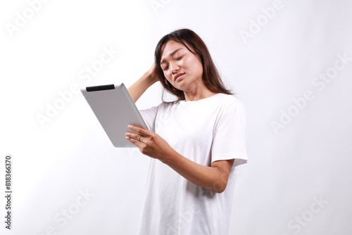 Attractive young asian woman holding a digital tablet while standing over white background with confused face expression © pakWw