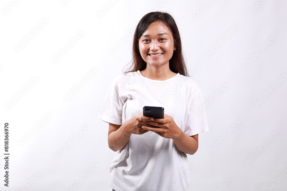Smiling pleasant young asian woman standing using mobile phone while looking directly to the camera. Isolated on white Smiling pleasant young asian woman standing using mobile phone while looking directly to the camera. Isolated on white