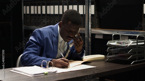Black policeman conducts confidential investigation, analyzes evidence and makes crucial phone calls. African american law officer uses telephone to collect classifed witness statements and clues. photo