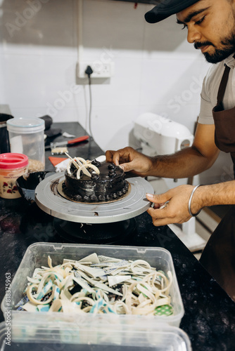 Attractive Indian male chef decorates candied chocolate cake in his kitchen. Sweet desserts,Bakery. 