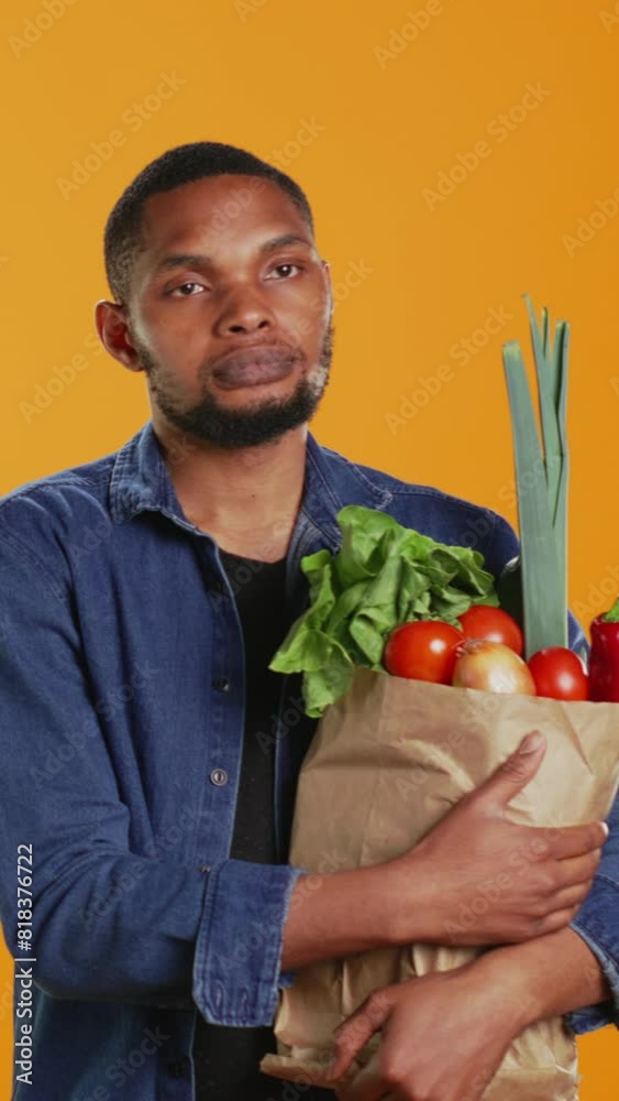Vertical Video Portrait of african american guy holding a paper bag full of bio food, buying organic locally grown fruits and vegetables. Confident vegan person supporting healthy eating and zero Vertical Video Portrait of african american guy holding a paper bag full of bio food, buying organic locally grown fruits and vegetables. Confident vegan person supporting healthy eating and zero