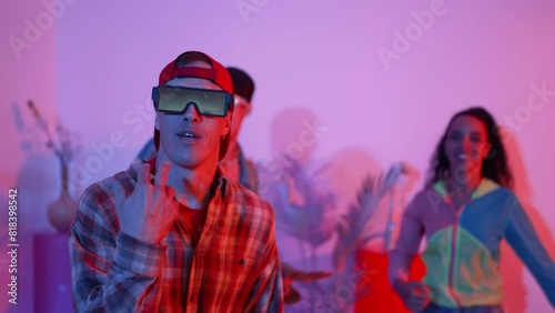 Attractive dancer moving along hip hop music with diverse friend dancing and supporting performance. Professional multicultural people wearing stylish cloth at studio with neon light. Regalement. photo