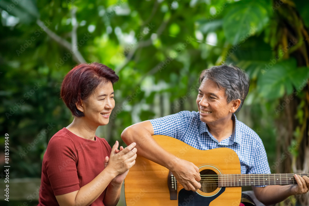 Fototapeta premium Middle aged couple playing guitar while relax sitting on bench in backyard.