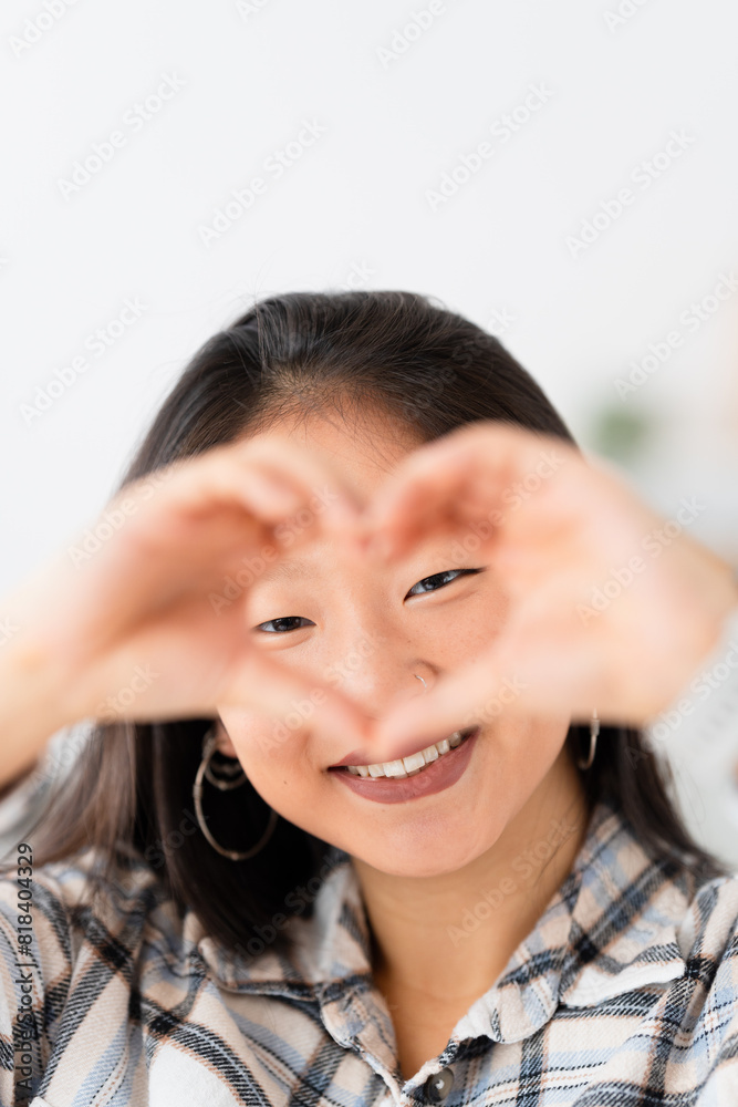 Vertical photo of an asian woman gesturing heart with hands smiling at camera Vertical photo of an asian woman gesturing heart with hands smiling at camera