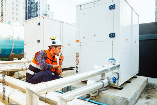 HAVC refrigeration system mechanic daily inspection refrigeration equipment on the roof building checking pressure and electrical control systems using radio communications to report technician team.