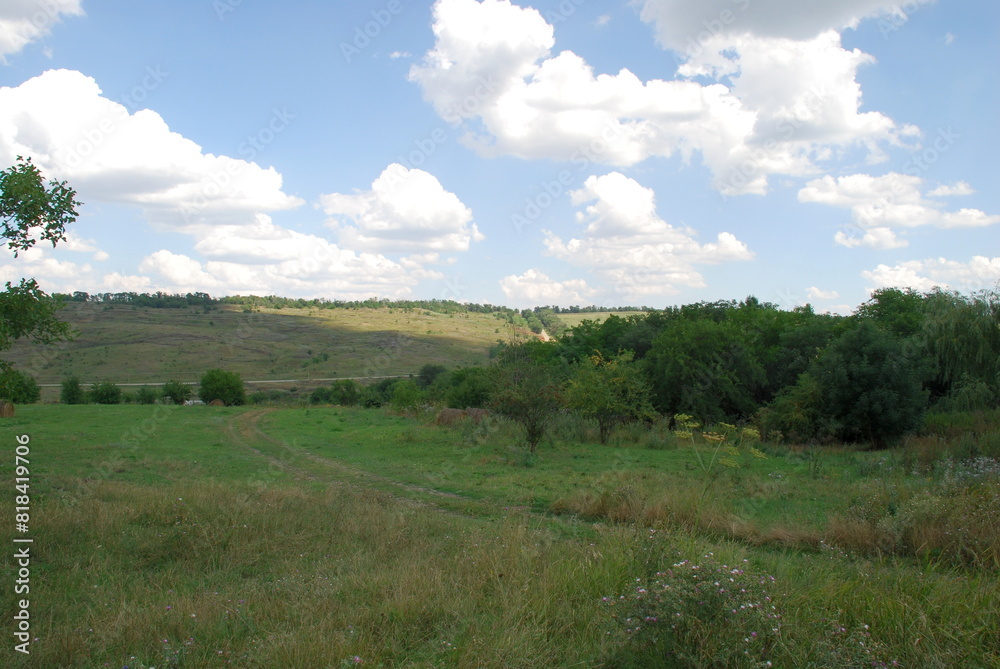 Countryside from a hilltop. Under a bright sky with white cumulus clouds, a rural landscape with wide fields, hills and forest plantations is visible, and a road is visible. Steppes of the Caucasian U Countryside from a hilltop. Under a bright sky with white cumulus clouds, a rural landscape with wide fields, hills and forest plantations is visible, and a road is visible. Steppes of the Caucasian U
