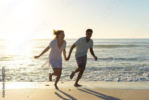 At beach, biracial couple holding hands, running along shore photo