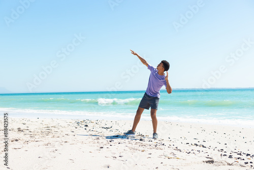 At beach, biracial young man throwing frisbee, wearing purple shirt