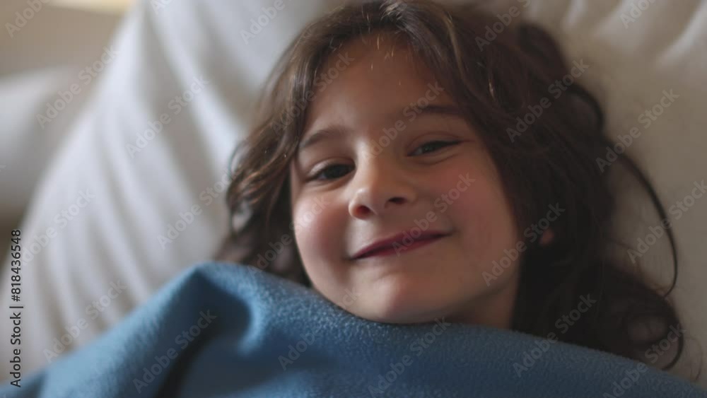 A young boy cheerfully smiling, wrapped in a blanket, relaxing on a couch during the day. A young boy cheerfully smiling, wrapped in a blanket, relaxing on a couch during the day.