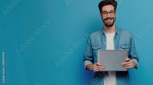 Photo of handsome smiling man holding laptop isolated on blue color background, eyes clearly visible and skin texture clean photo