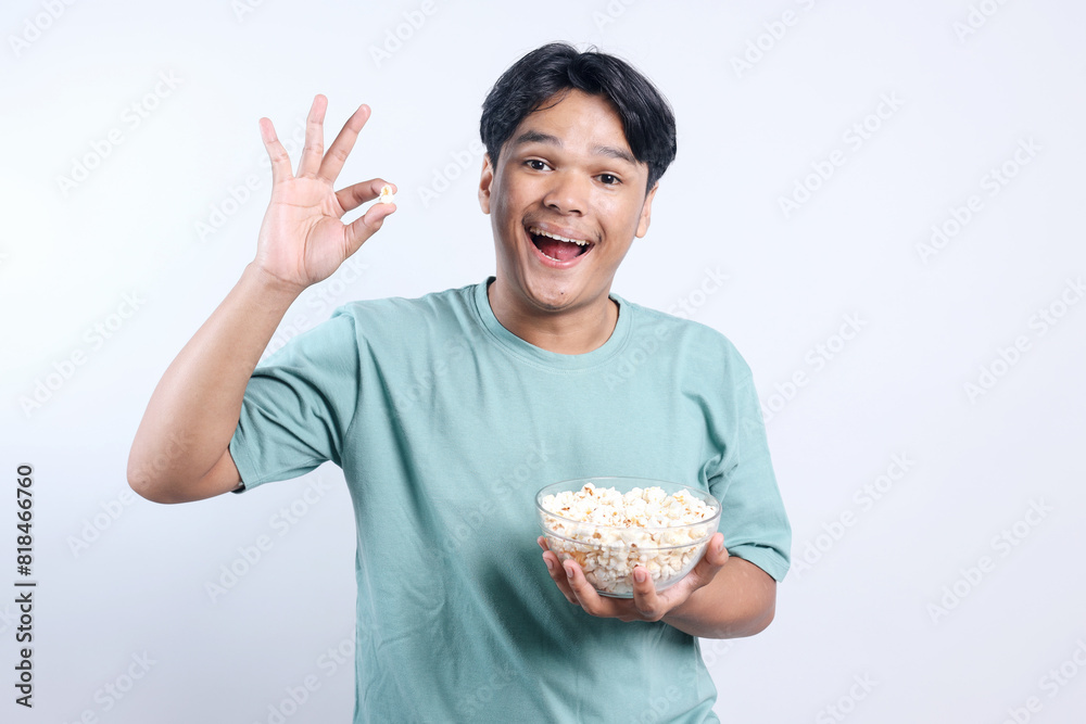 Potrait Of Cheerful Young Asian Guy Showing Ok Sign While Holding Popcorn Bowl Isolated On White Background