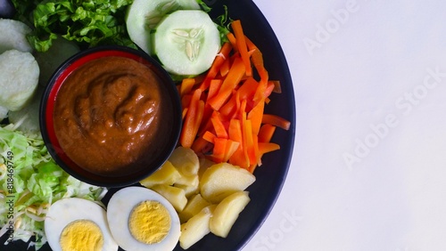 Gado-gado served on a plate, isolated white, Indonesian salad containing boiled vegetables and potatoes, boiled eggs, fried tofu tempeh, lontong and melinjo chips, served with peanut-cashew sauce.  photo