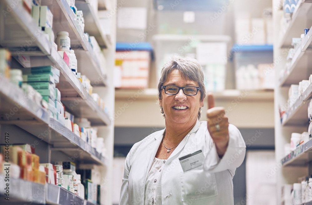 Mature, pharmacist or portrait of happy woman with thumbs up in healthcare clinic, pharmacy or drugstore. Like sign, yes gesture or confident smile by shelf for pills medication or medicine approval Mature, pharmacist or portrait of happy woman with thumbs up in healthcare clinic, pharmacy or drugstore. Like sign, yes gesture or confident smile by shelf for pills medication or medicine approval