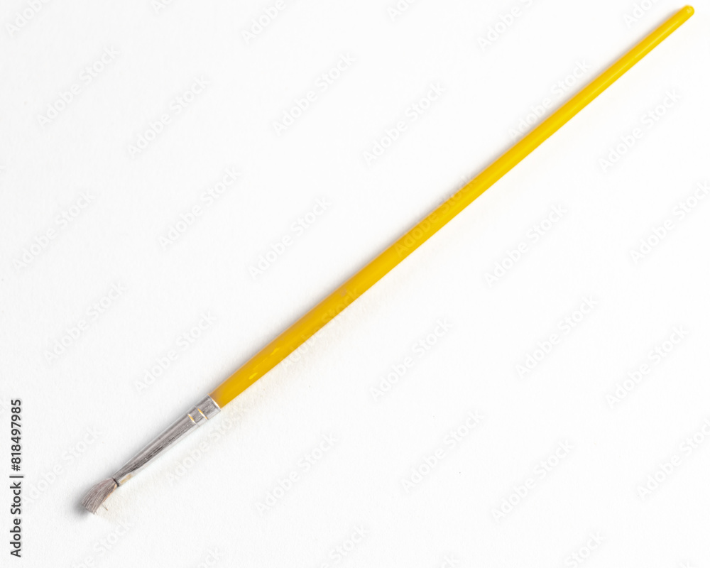 Small, yellow, used painting brush on white paper background. Small, yellow, used painting brush on white paper background.