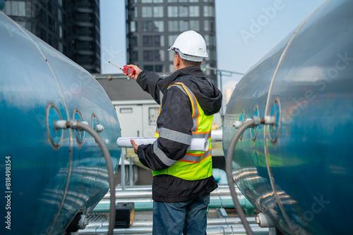 Engineer inspects water heater pump system and hot water tank on industrial roof