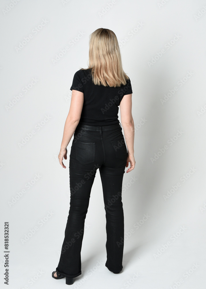 Full length portrait of beautiful blonde woman wearing modern black shirt and leather pants. Confident standing pose walking away from camera, silhouetted on white studio background. Full length portrait of beautiful blonde woman wearing modern black shirt and leather pants. Confident standing pose walking away from camera, silhouetted on white studio background.