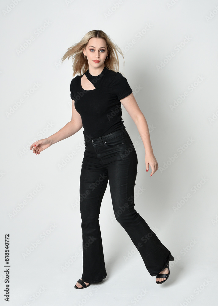Full length portrait of beautiful blonde woman wearing modern black shirt and leather pants. Confident standing pose with gestural hands presenting, silhouetted on white studio background. Full length portrait of beautiful blonde woman wearing modern black shirt and leather pants. Confident standing pose with gestural hands presenting, silhouetted on white studio background.