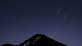 A mountain silhouette with a shooting star streaki