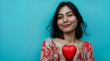 A young romantic woman holds a red heart in her hands. Symbol of love and friendship on blue background.