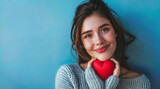 A young romantic woman holds a red heart in her hands. Symbol of love and friendship on blue background.
