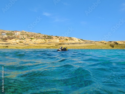 Island of Gozo, Mediterranean sea, rugged shoreline and stone, scuba diver on the surface. Scuba diving trip, diver close to the shore. Travel picture, sea surface.