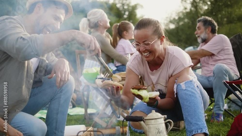 Dad puts freshly grilled meat in bread for family members while camping