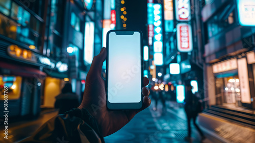 hand holding a smartphone in a busy city street at night.