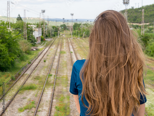 A girl in a blue t-shirt stands on a bridge over railway tracks