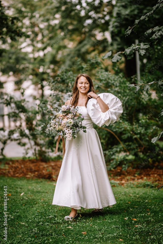 Riga, Latvia, - August 26, 2024 - Bride in white dress with large bouquet in park. Riga, Latvia, - August 26, 2024 - Bride in white dress with large bouquet in park.