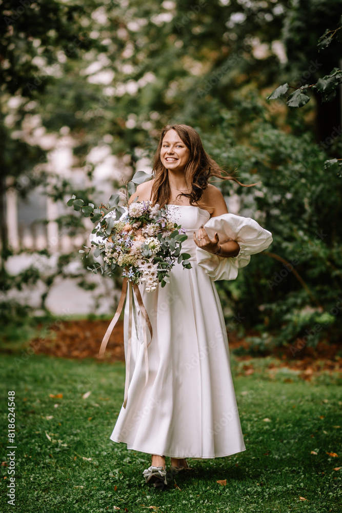 Riga, Latvia, - August 26, 2024 - Bride smiling, holding a large bouquet, walking in a lush park. Riga, Latvia, - August 26, 2024 - Bride smiling, holding a large bouquet, walking in a lush park.