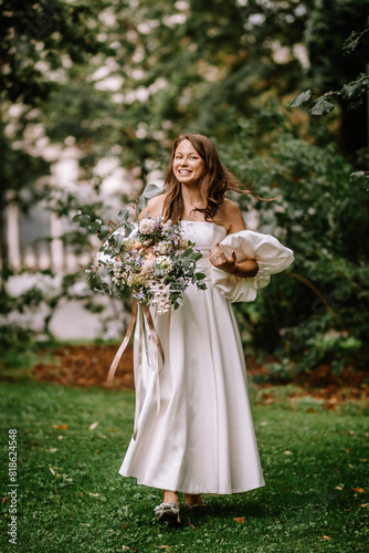 Riga, Latvia, - August 26, 2024 - Bride smiling, holding a large bouquet, walking in a lush park. © Raivo