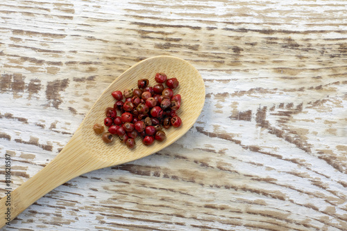 Red or pink peppercorns on wooden spoon on grey textured cutting board background