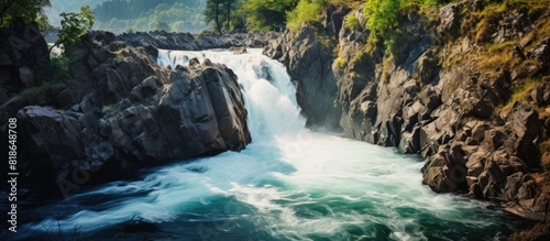 A picturesque waterfall cascades from a rugged cliff gracefully joining a river adorned with scattered rocks Copy space image