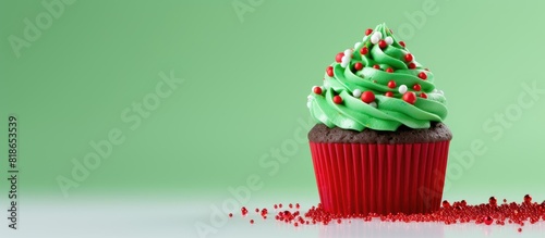 A festive Christmas themed cupcake with green frosting vibrant sprinkles and decorative accents placed in a red cup on a clean white background Ample copy space available
