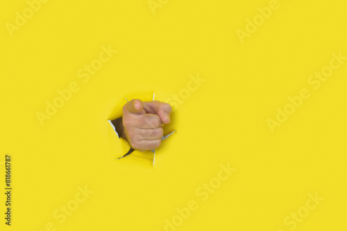 Male hand pointing to the front emerging from a hole in a torn paper background. photo