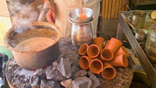 Close up indian man making a pot of tandoori tea over hot coals with clay earthenware cups heating on the side to serve in Jaipur, Delhi, Lucknow