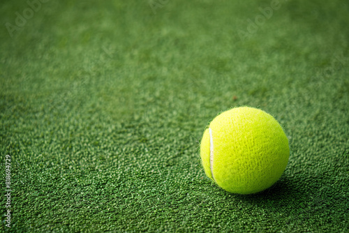 A tennis ball is sitting on a green grass field. The ball is yellow and has a fuzzy texture © Image-Love