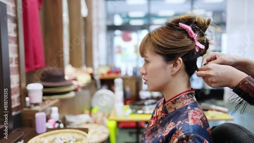 Young Taiwanese woman in blue floral cheongsam getting hair and makeup done at vanity table in Wanhua District, Taipei City. Slowmotion photo