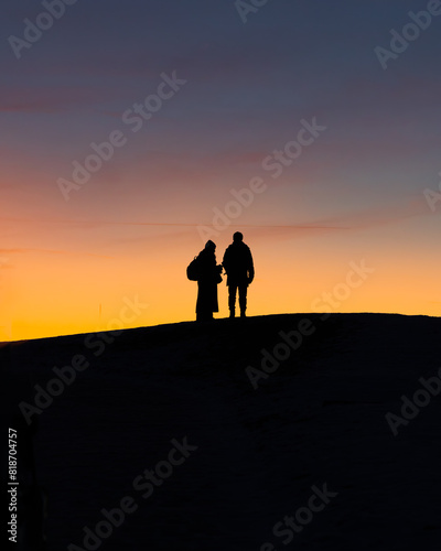 Two people standing on a hill watching the sunset