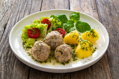 Cooked meatballs in dill sauce with boiled potatoes and fresh vegetables on wooden table 