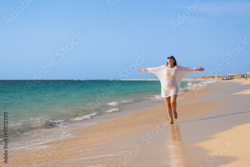 Beautiful woman with arms raised and outstretched walking on sunny beach 