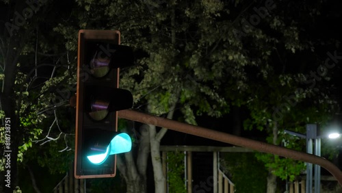 Time lapse: vertical traffic light quickly turns green, yellow and red against green tree leaves at night - close up view. Timelapse, urban, warning and regulation concept