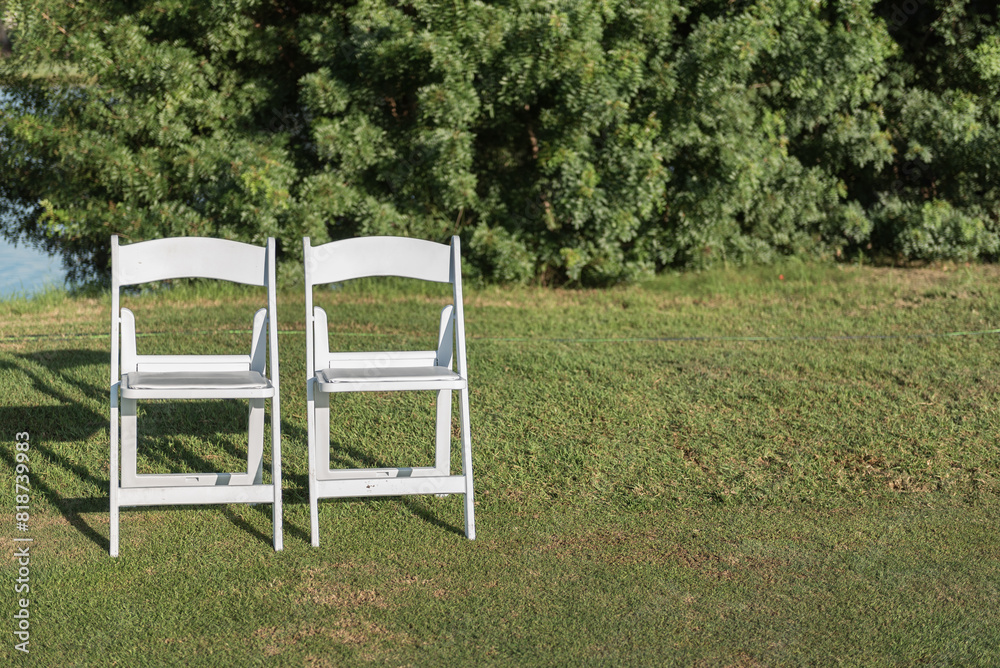 Two chairs placed on a green lawn set up for an outdoor wedding ceremony Two chairs placed on a green lawn set up for an outdoor wedding ceremony