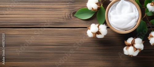 A flat lay of organic cosmetic products featuring cotton flower green leaves and a wooden background Ample copy space provided