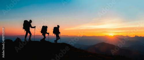 Three people are hiking up a mountain, with the sun setting in the background. The silhouettes of the hikers are emphasized by the contrast of the bright sun against the dark mountainside